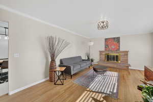 Living room with light wood-style floors, a stone fireplace, and crown molding