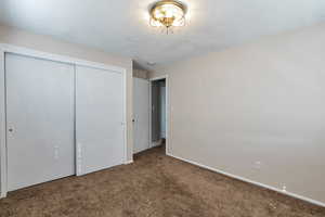 Unfurnished bedroom featuring a closet, dark colored carpet, and a textured ceiling