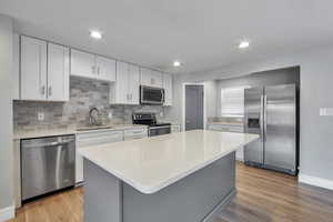 Kitchen featuring stainless steel appliances, light wood-type flooring, a kitchen island, light stone counters, and recessed lighting