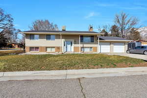 Split foyer home with brick siding, a front yard, a chimney, concrete driveway, and covered porch