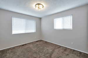 Empty room featuring dark carpet and a textured ceiling