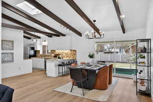 Dining area featuring vaulted beams and a statement chandelier light. Natural light from the skylight bathes the seamless light-toned flooring, highlighting the room's height and open-concept design.