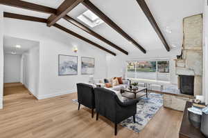 Living area with light wood-style floors, vaulted beam ceiling, a stone fireplace, and a skylight