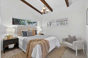 Bedroom #2 with soft neutral carpet flooring, multiple windows, vaulted ceiling with beams, and a chandelier.