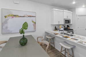 Kitchen featuring a kitchen bar, white cabinets, stainless steel appliances, and light wood finished floors