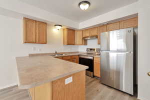 Kitchen featuring stainless steel appliances, a peninsula, light countertops, light wood-style floors, and a textured ceiling