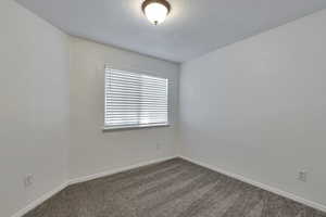 Spare room featuring dark colored carpet and a textured ceiling