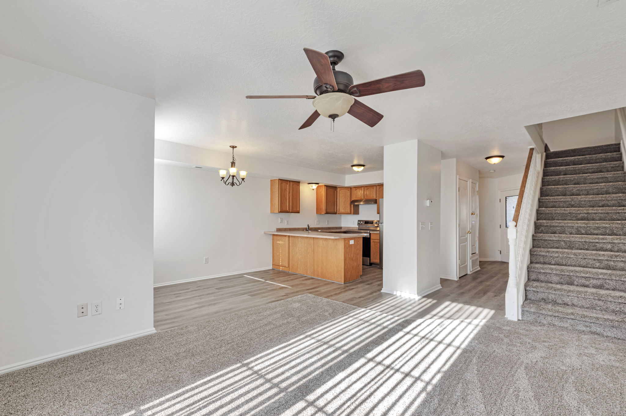 Unfurnished living room featuring light colored carpet, suspended lighting, and a ceiling fan