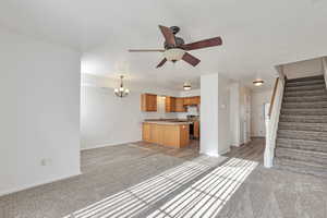 Unfurnished living room featuring light colored carpet, suspended lighting, and a ceiling fan