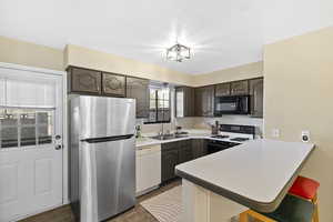 Kitchen featuring a breakfast bar area, freestanding refrigerator, gas range, dark wood finish cabinets, and a peninsula