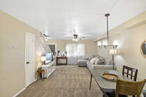 Carpeted living area featuring ceiling fan and stairway