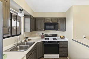 Kitchen featuring range with gas cooktop, light countertops, black microwave, and dark wood finish cabinetry