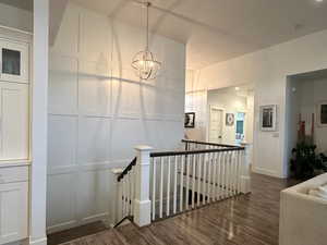 Corridor with an upstairs landing, wood-style floors, hanging lights, and a custom wall molding