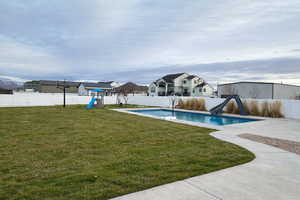 View of a fenced backyard with a swimming pool with a water slide and  diving board, a 1/2 court basketball court, a Lifetime play gym and concrete patio areas