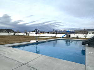 View of a fenced backyard with a swimming pool with a water slide and  diving board, a 1/2 court basketball court, a Lifetime play gym, large yard and view of mountains
