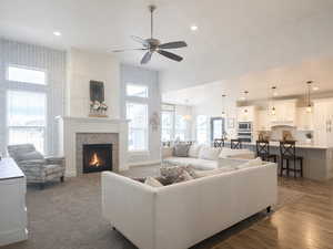Living room featuring ceiling fan, high ceilings, recessed lighting, a fireplace, wood-style floors and multiple windows