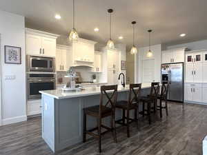 Kitchen with stainless steel appliances, white cabinets, wood-type flooring, a spacious island, and a walk-in pantry