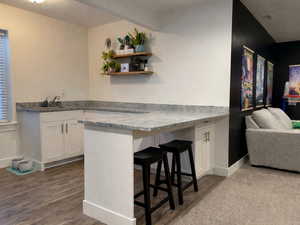 Kitchenette featuring a peninsula, white cabinetry, a breakfast bar, sink, mini-fridge cabinet opening, and granite countertops