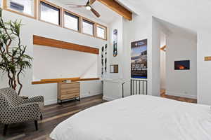 Bedroom featuring dark wood finished floors, ceiling fan, a warm lit fireplace, and lofted ceiling