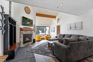 Living room with dark wood finished floors, a stone fireplace, beamed ceiling, and recessed lighting