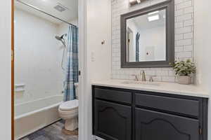 Bathroom with vanity, dark wood-type flooring, backsplash, and shower / bathtub combination with curtain