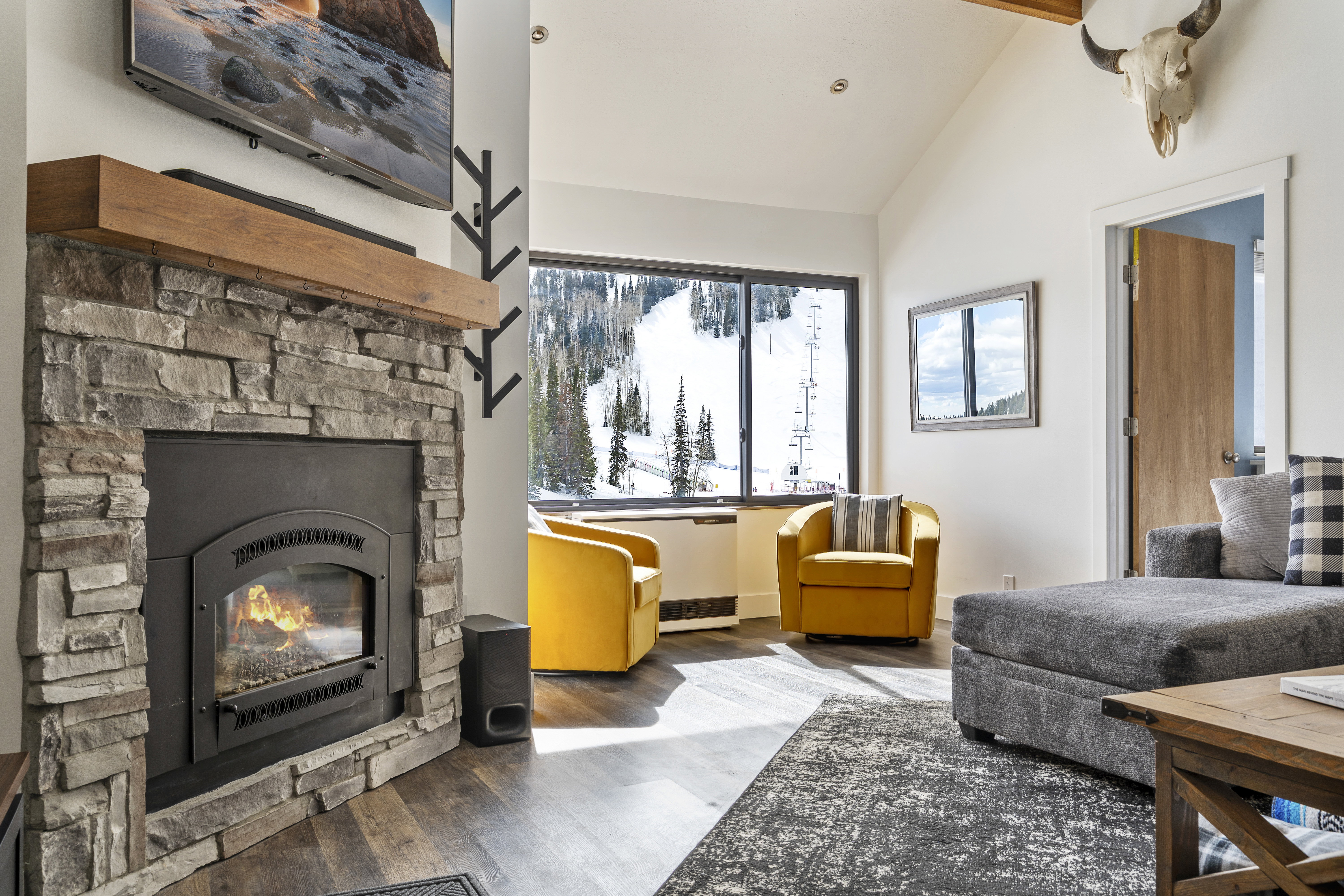 Living room featuring wood finished floors, a stone fireplace, and lofted ceiling with beams