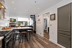 Kitchen featuring a peninsula, exhaust hood, a breakfast bar, dark wood-style flooring, and a fireplace