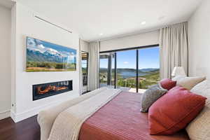 Bedroom with access to outside, a glass covered fireplace, dark wood-style floors, a water and mountain view, and recessed lighting