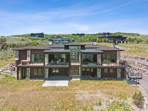 Rear view of house with a standing seam roof, stone siding, a patio area, and a balcony