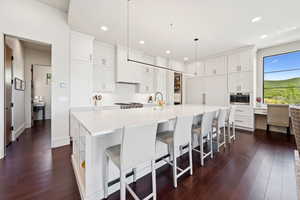 Kitchen featuring white cabinets, a kitchen bar, dark wood-style floors, a large island, and decorative light fixtures