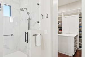 Full bath featuring a marble finish shower, dark wood-style floors, and a spacious closet