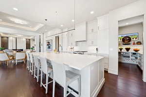 Kitchen featuring white cabinets, a spacious island, a breakfast bar area, dark wood finished floors, and light stone counters