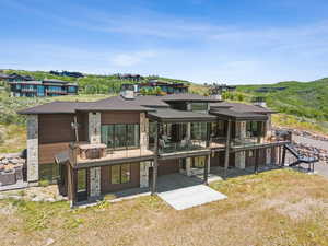 Rear view of property featuring stone siding, an attached garage, a patio, a balcony, and a metal roof
