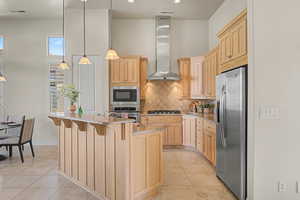 Kitchen with light wood finish cabinets, a kitchen breakfast bar, a center island with sink, stainless steel appliances, and light tile patterned floors