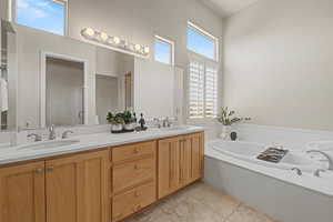 Full bath with healthy amount of natural light, double vanity, a bath, and light tile patterned floors