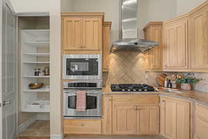 Kitchen featuring stainless steel appliances, light stone counters, light wood finish cabinetry, and decorative backsplash