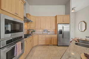 Kitchen featuring stainless steel appliances, light wood finish cabinetry, light stone countertops, and decorative backsplash