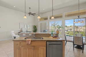 Kitchen featuring stainless steel dishwasher, decorative light fixtures, light stone countertops, light tile patterned floors, and an island with sink