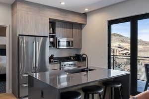 Kitchen featuring high end appliances, dark stone countertops, modern cabinets, a breakfast bar area, and open shelves