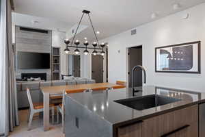 Kitchen featuring open floor plan, dark stone countertops, a center island with sink, a fireplace, and modern cabinets