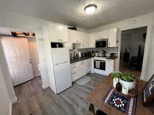 Unit 4365 Kitchen with dark countertops, white appliances including dishwasher, white cabinetry, laminate flooring, a textured ceiling, and decorative backsplash