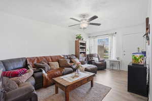 Living area with light wood-style floors, a textured ceiling, and a ceiling fan