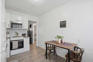 Kitchen with white cabinets, white appliances, light wood-style flooring, and backsplash