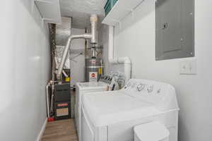 Laundry area featuring electric panel, washer and dryer, a textured ceiling, water heater, and wood finished floors