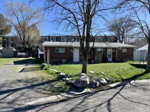 View of front facade featuring a carport, brick siding, a storage shed, a front lawn, and driveway