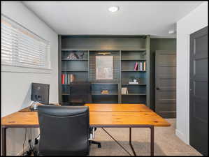Office area with light carpet and custom built-in shelving