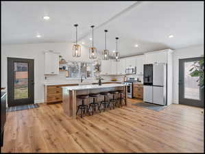 Kitchen with two tone cabinetry, stainless steel appliances, open shelves, light wood-style floors, and pendant lighting