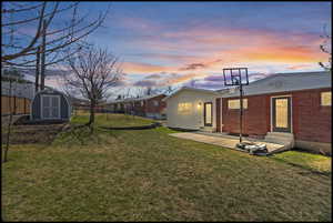 Back of property at dusk with entry steps, a fenced backyard, a storage unit, and brick siding