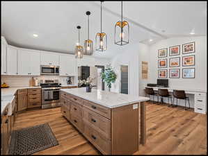 Dual tone kitchen with two tone cabinetry, stainless steel appliances, light stone countertops, pendant lighting, and a center island