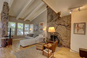Living room with a stone fireplace, light wood-type flooring, rail lighting, and lofted ceiling
